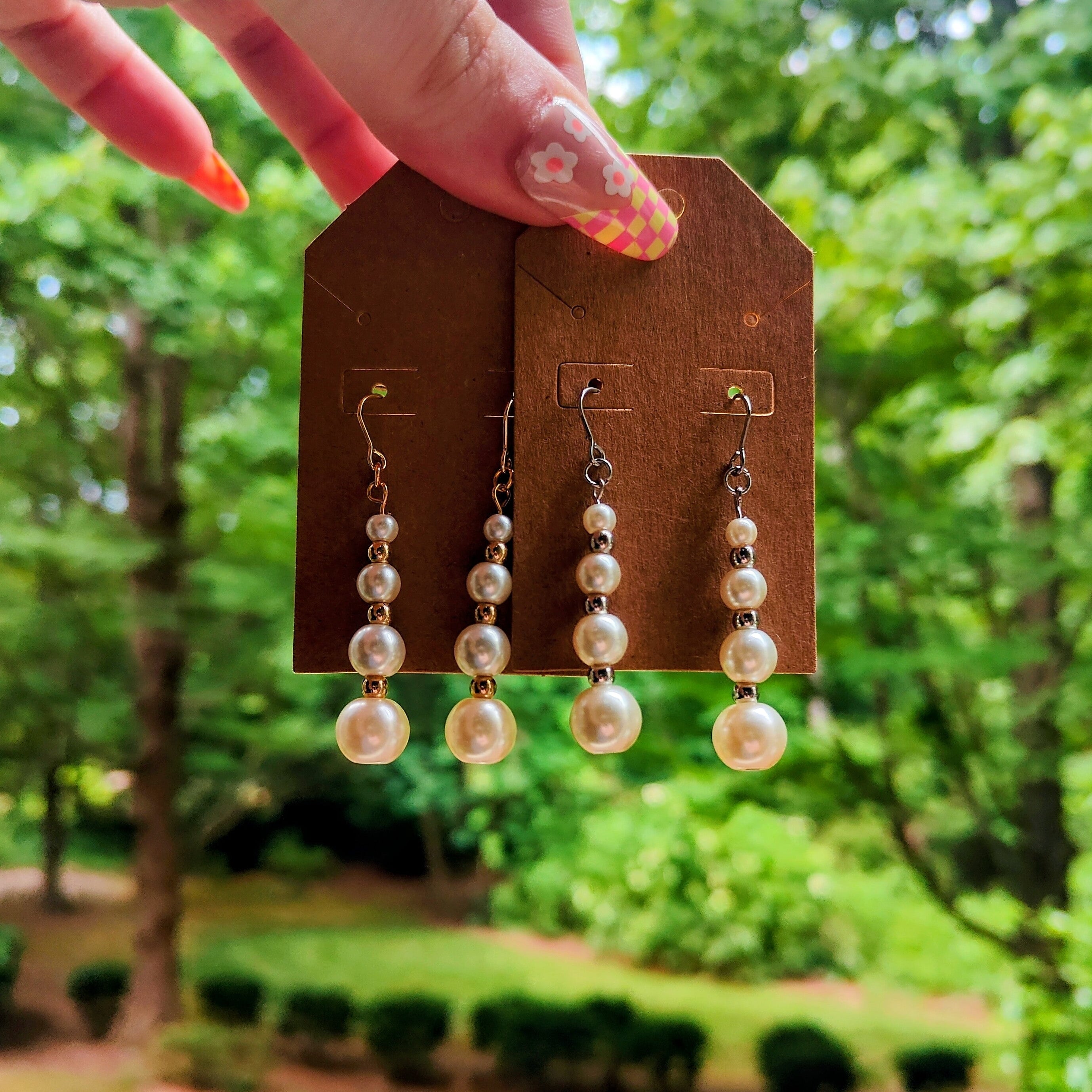 Pearl drop earrings on a display card held by a hand with a garden background