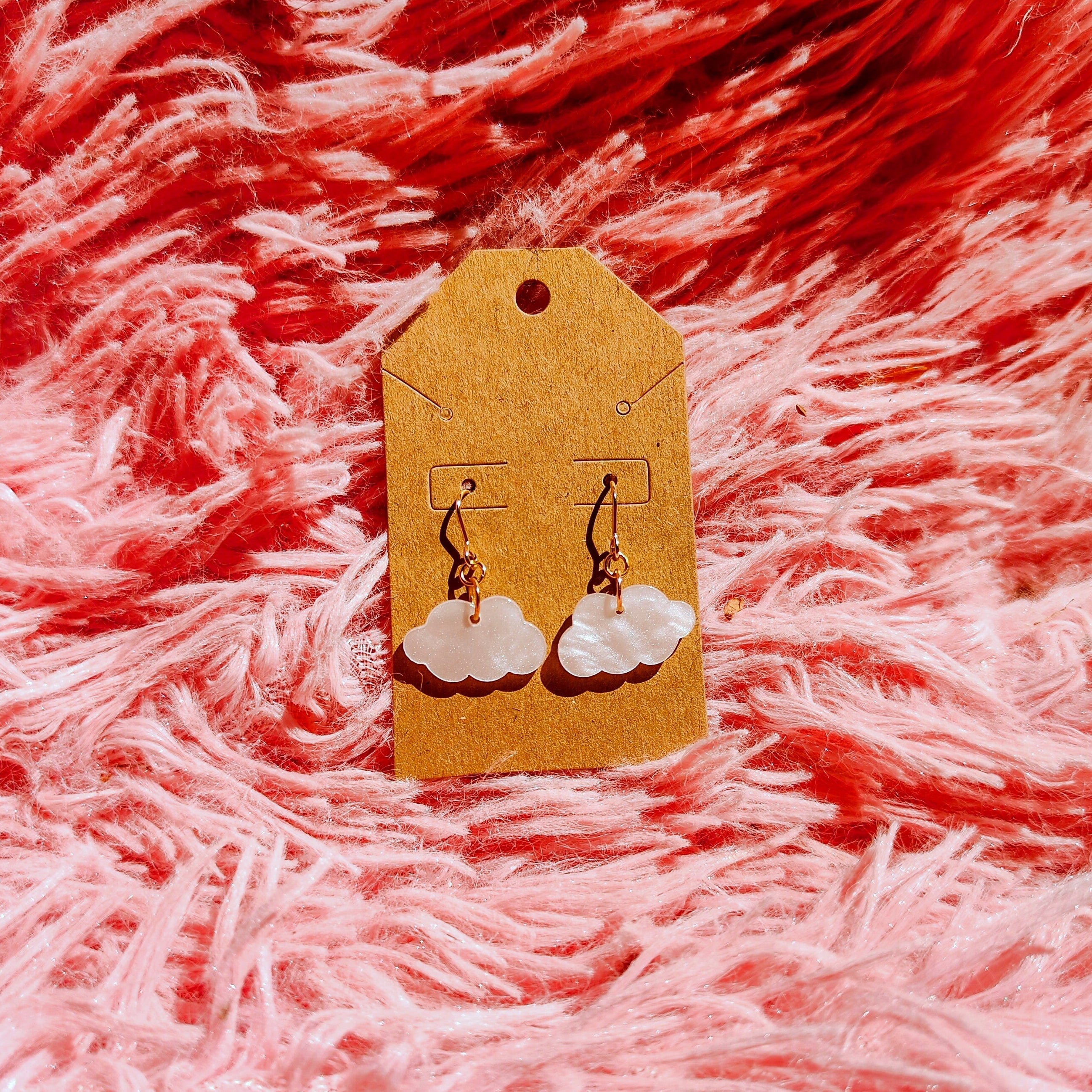 Gold earrings with cloud charm and a gold earrings post on a pink fluffy fabric background