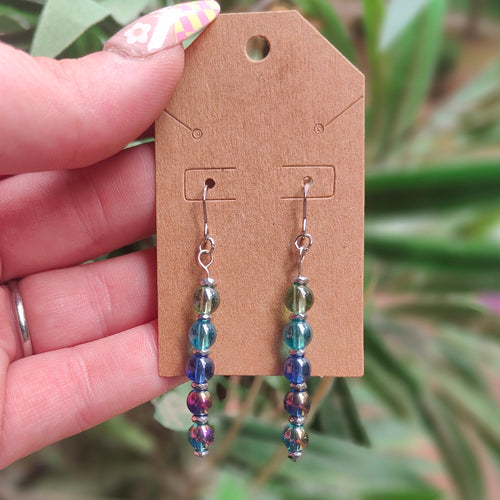 Beaded earrings on a cardboard earring card held by a hand with a blurred green plant background