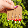 Hand holding a card with mushroom-shaped earrings against a green leafy background