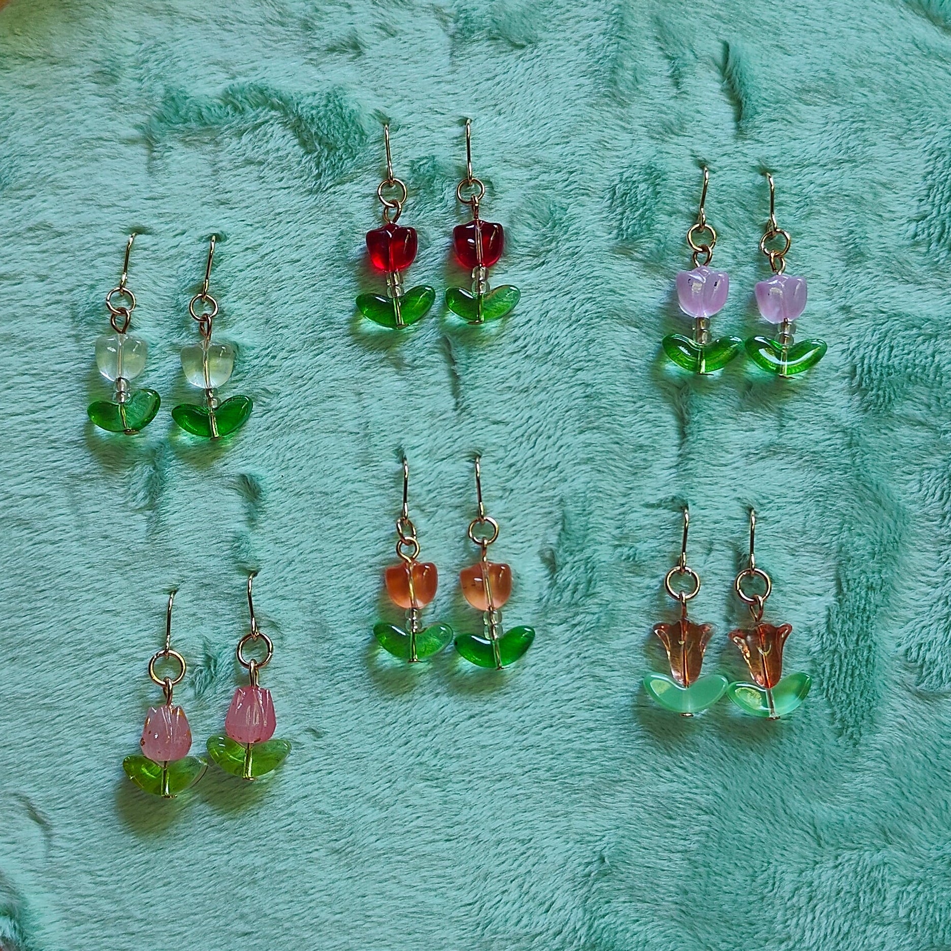Set of earrings displayed on a green embroidery hoop against a pink textured background