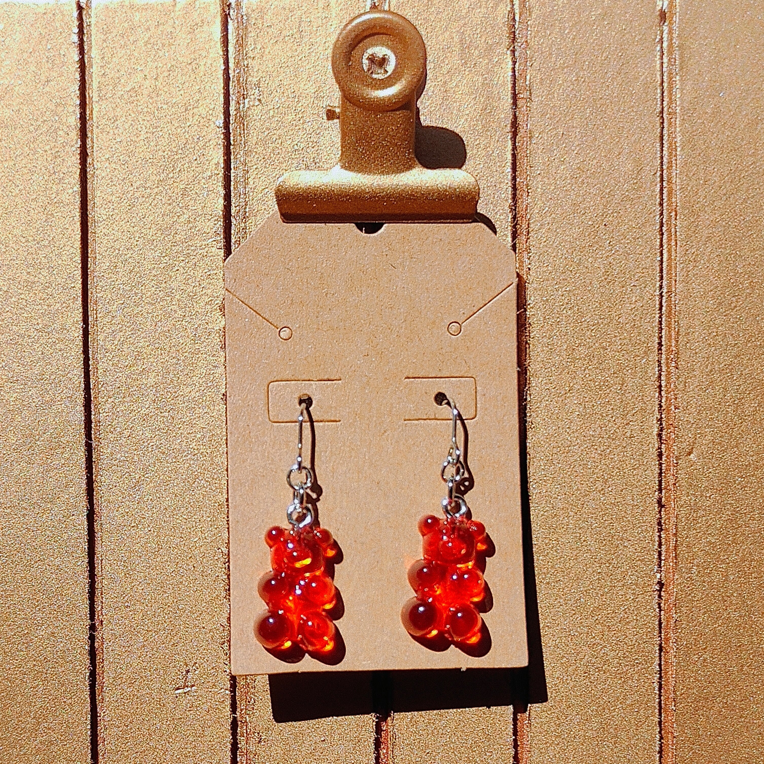 Red gummy bear-shaped earrings on a cardboard backing with a clip.
