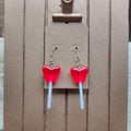 Heart-shaped lollipop earrings on a cardboard display with a background