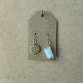 Cookie and milk earrings on a cardboard tag against a beige background