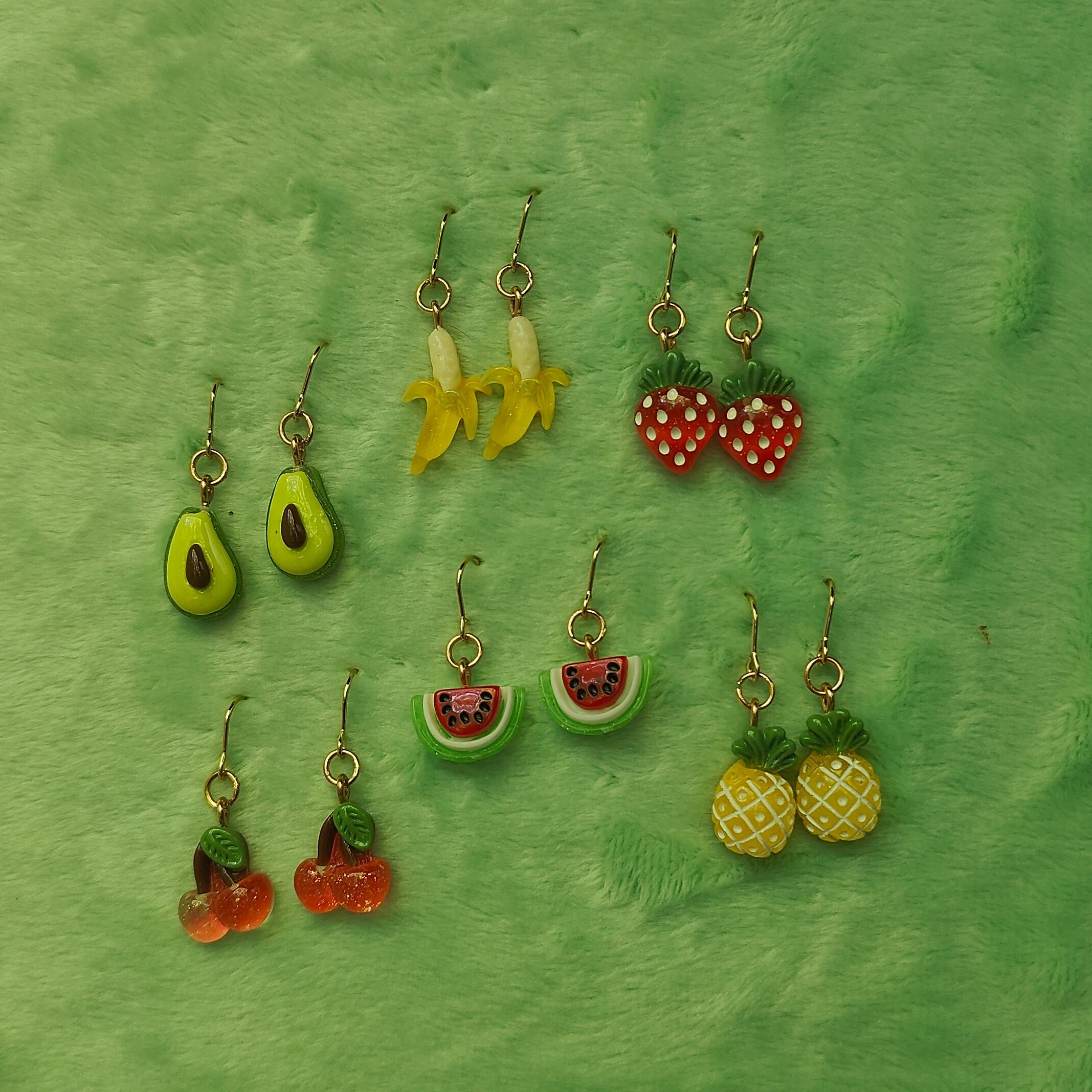 Collection of fruit-themed earrings on a green fabric background