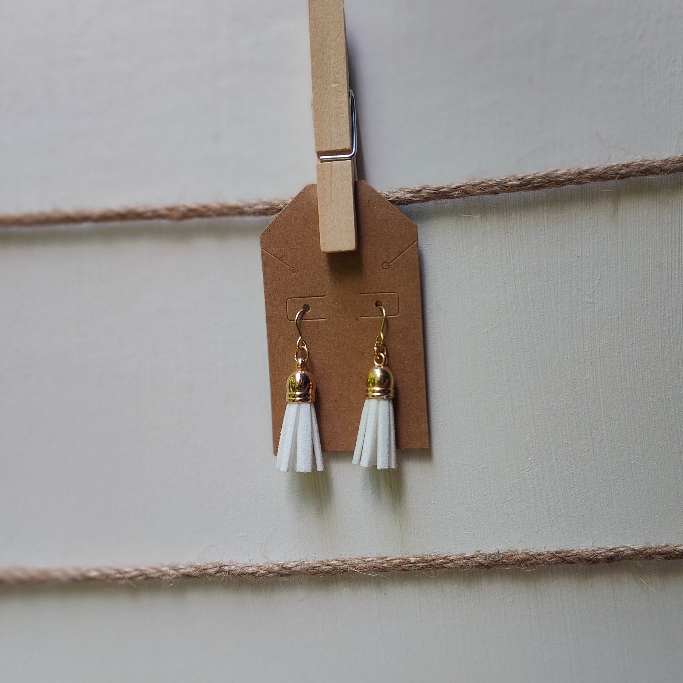 Pair of earrings with white tassels hanging on a string with a clothespin.