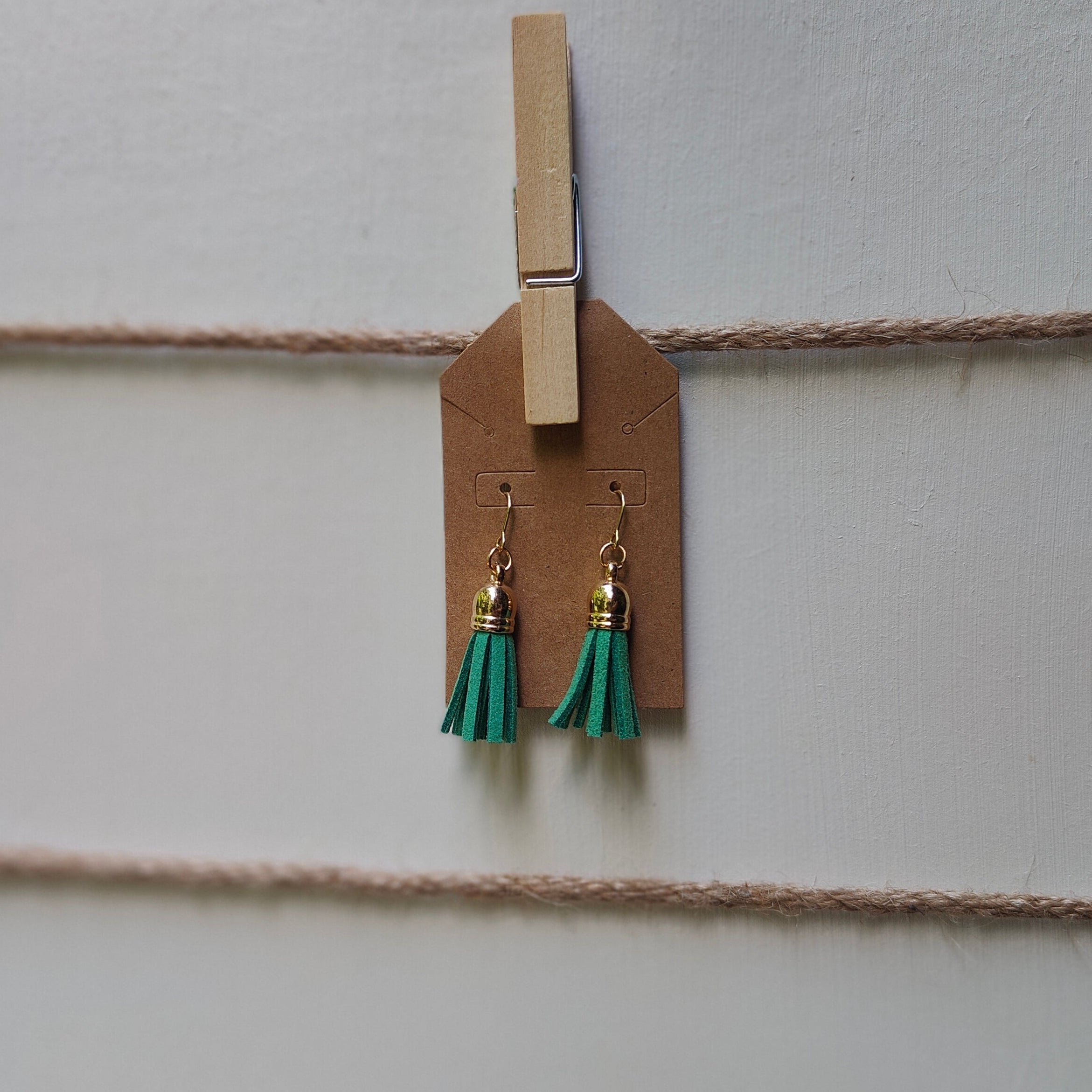 Pair of earrings with green tassels hanging from a wooden peg on string.