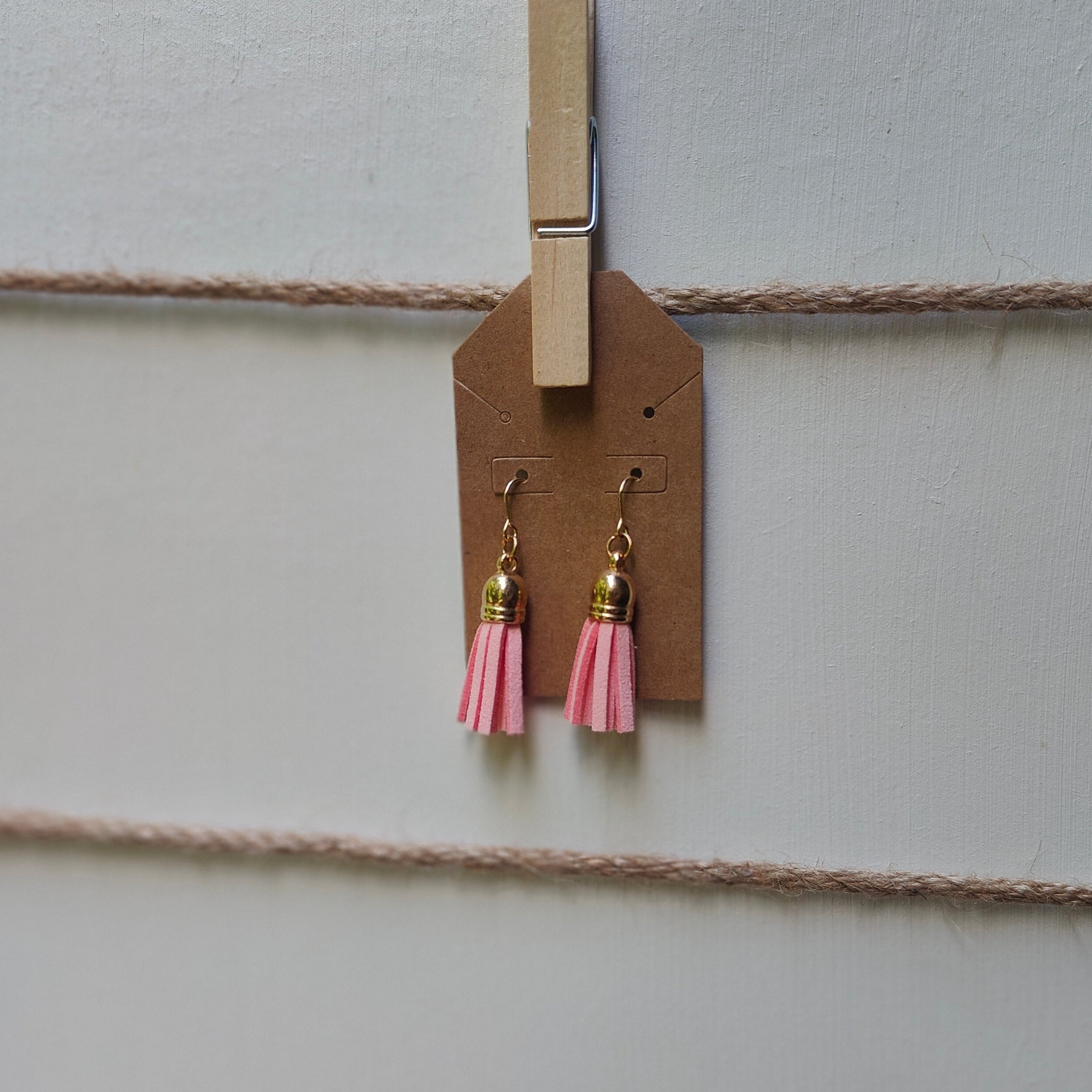Pink tassel earrings hanging from a clothespin on a string against a neutral background