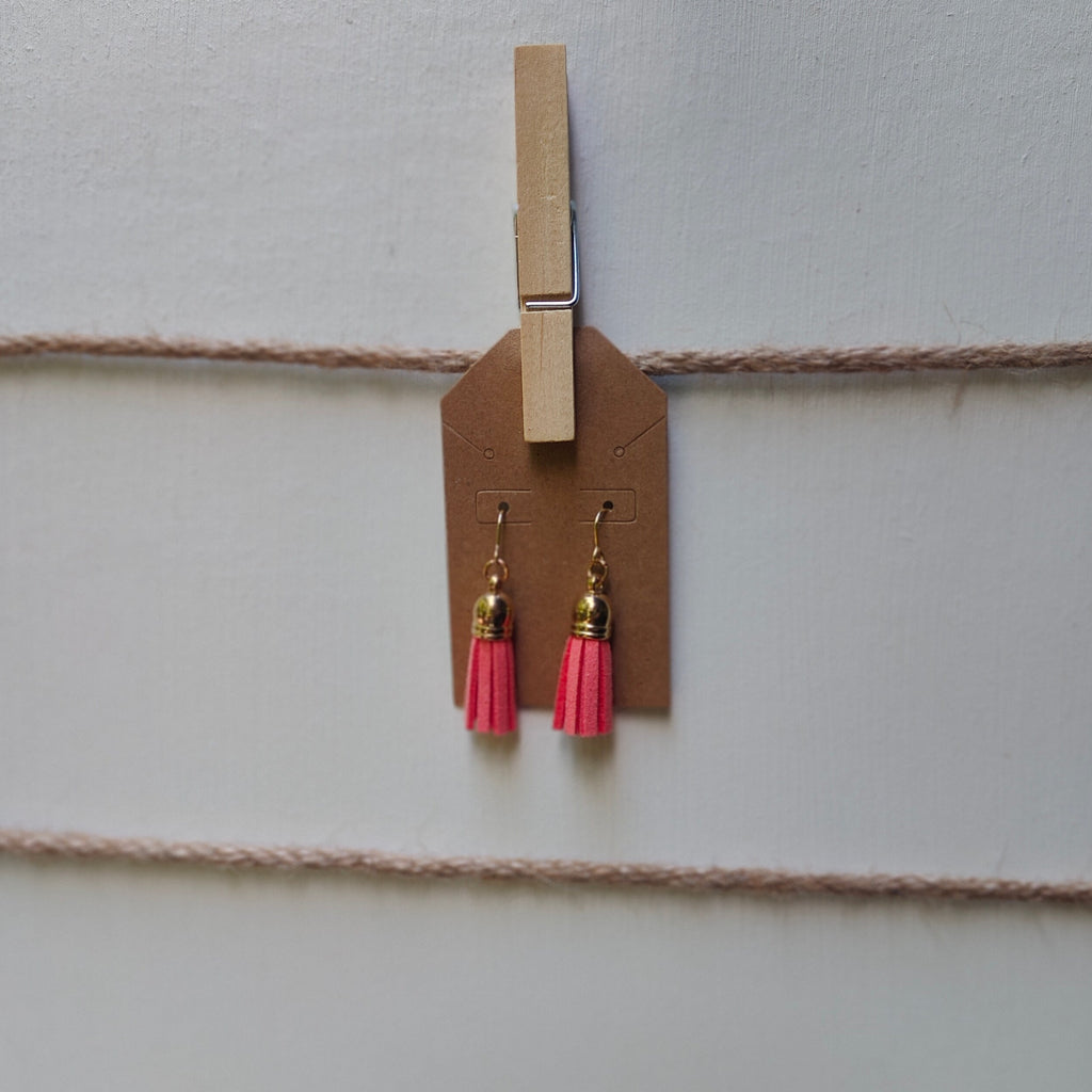 Pink tassel earrings hanging from a clothespin on a string against a light background