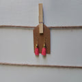 Pink tassel earrings hanging from a clothespin on a string against a light background