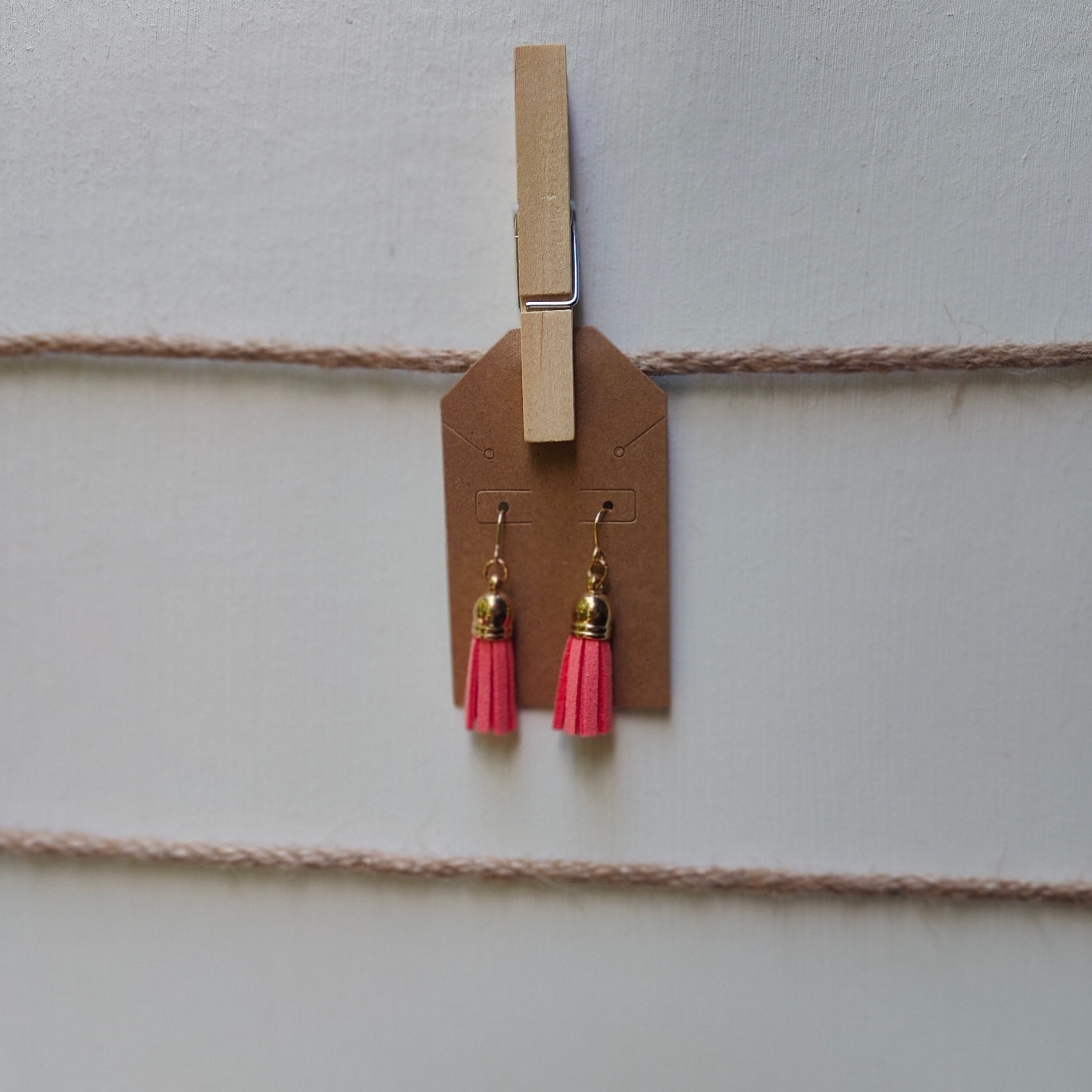 Pink tassel earrings hanging from a clothespin on a string against a light background